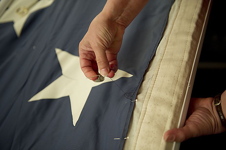 ** FILE ** A woman stitches some of the blue fabric of the official 9/11 American flag during a stitching ceremony in the Russell Senate Office Building in Washington on Thursday, July 14, 2011. This American flag, which was flying just south of the World Trade Center in New York City on Sept. 11, 2001, is making its way around the country and being stitched back together. The goal is to have the flag completed by this Sept. 11, 2011, in time for the 10th anniversary. The finished flag will be on display at the official 9/11 Memorial in New York City. (The Washington Times)