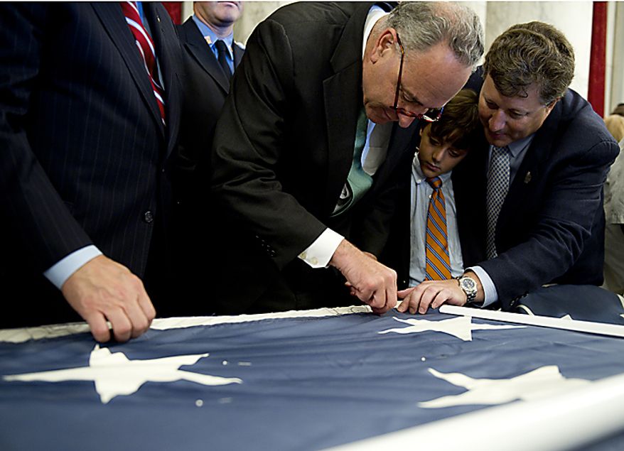 Sen. Charles Schumer (D-N.Y.), left, stitches on the official 9/11 National flag while Jeff Parness, founder and chairman of the New York Says Thank You Foundation and his son, Josh, look on. The flag was at the Russell Senate Office Building in Washington, D.C., on Thursday, July 14, 2011. This flag was flying south of the World Trade Center in New York City on Sept. 11, 2001, and now it is making its way around the country and is being stitched back together by Americans. When it is completed, it will hang in the official Sept. 11 memorial in New York City. (Barbara L. Salisbury/The Washington Times)