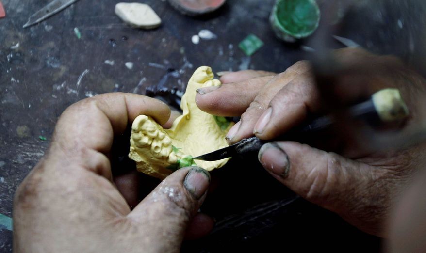 A Cuban man who did not want to be identified molds a tooth with wax before making a gold tooth. (Associated Press)