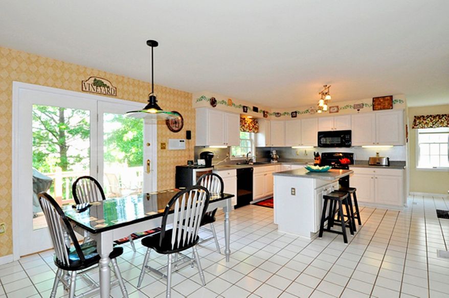 The kitchen features a center island that doubles as a breakfast bar, ceramic tile flooring, Corian counters and white cabinets.