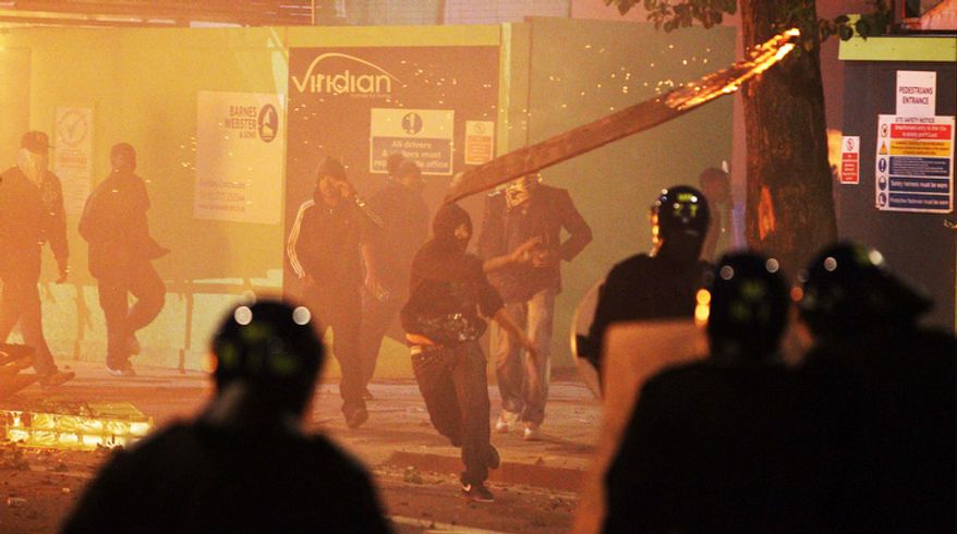 A rioter throws a burning wooden plank at police in Tottenham, north London Sunday Aug. 7, 2011, after members of a community, where a young man was shot dead by police, took to the streets to demand "justice." (AP Photo/PA, Lewis Whyld)