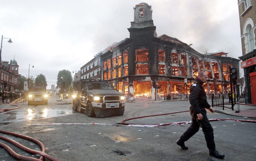 Police vehicles drive past a fire in a building in Tottenham. One police officer was hospitalized and seven others were injured during riots when a north London suburb exploded in anger Saturday night. (AP Photo/Lewis Whyld/PA Wire)