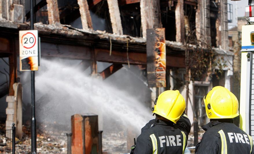 Firefighters look at a burned-out building in Tottenham, north London, still being damped down after a demonstration against the death of a local man turned violent and cars and shops were set ablaze. (AP Photo/Akira Suemori)