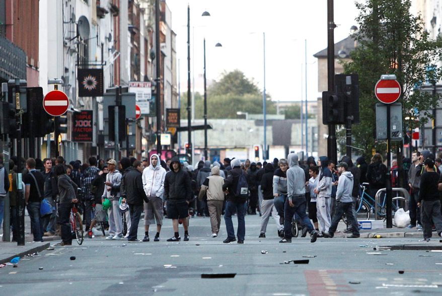 Crowds stand on Oldham street during civil disturbances in Manchester, England. Britain began flooding London's streets with 16,000 police officers Tuesday as rioting starting for a fourth night. (AP Photo/Jon Super).