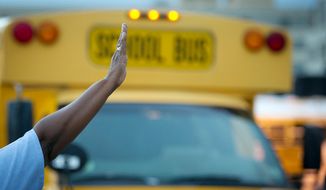 A crossing guard directs school buses on the first day of school year. (Rod Lamkey Jr./The Washington Times)