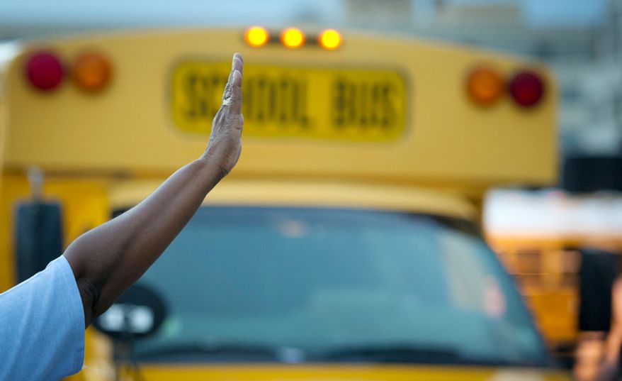 A crossing guard directs school buses on the first day of school year. (Rod Lamkey Jr./The Washington Times)
