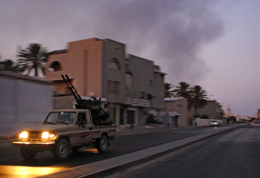 An armored vehicle speeds on the outskirts of Tripoli as huge smoke rises over the downtown area on Aug. 22, 2011. (Associated Press)