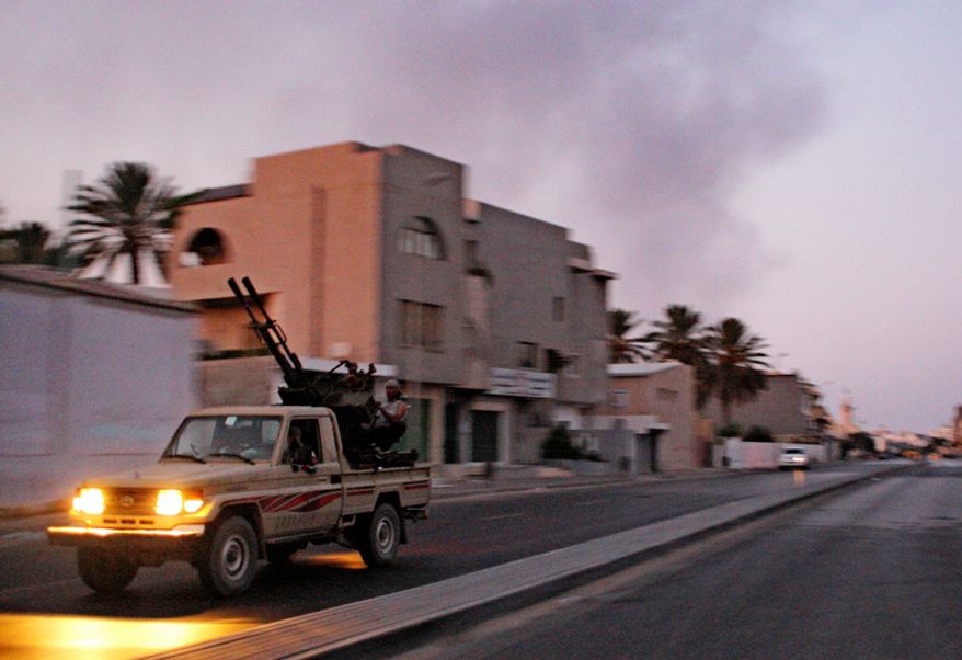 An armured vehicle speeds on the outskirts of Tripoli, as huge smoke rises over the downtown, late Monday, Aug. 22, 2011. Moammar Gadhafi's whereabouts remained unknown. (AP Photo/Sergey Ponomarev)