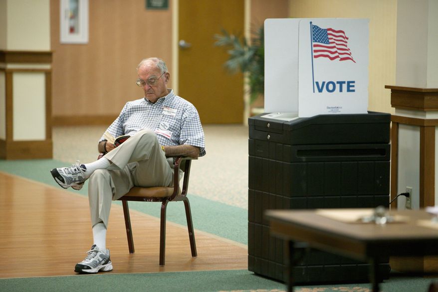 Election official Bob MacCallum reads a book while awaiting voters at the Greenspring retirement community in Springfield on Tuesday. (Andrew Harnik/The Washington Times)