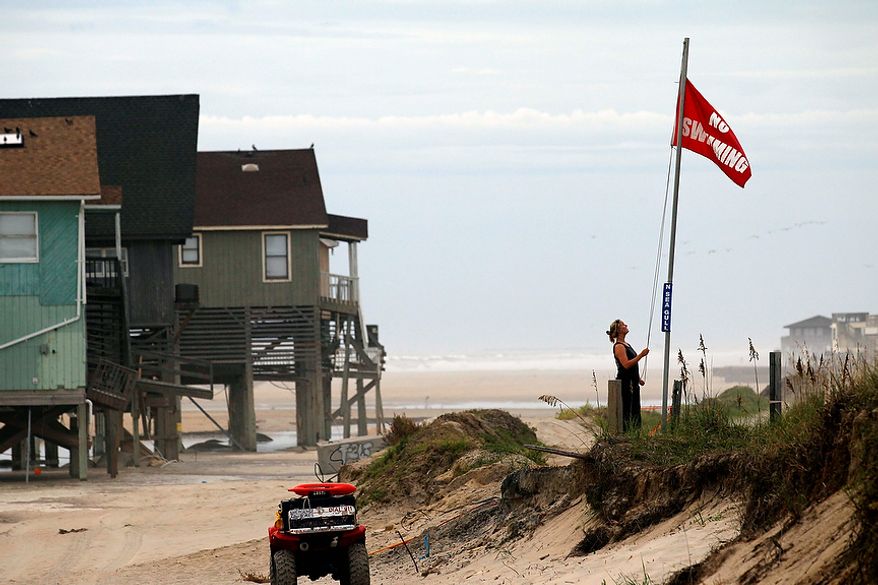 Erika Audfroid, a lifeguard with Nags Head Ocean Rescue, hoists a no swimming flag along the beach in Nags Head, N.C., Friday, Aug. 26, 2011 as hurrican Irene takes aim at the North Carolina coast. The full force of Hurricane Irene was still a day away from the East Coast but heightened waves began hitting North Carolina's Outer Banks early Friday. (AP Photo/Gerry Broome)