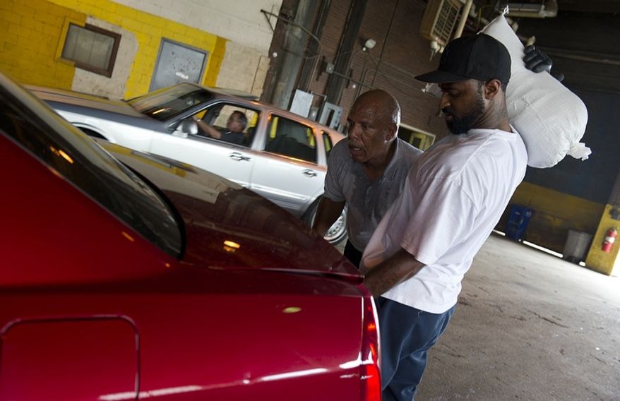Jerry Stanback (left), a general foreman with D.C.'s Department of Public Works, and Cameron Washington, a motor vehicle operator for the department, wait for a city resident to open his vehicle's trunk so they can place sandbags inside at the department headquarters in southeast Washington on Aug. 26, 2011, a day before Hurricane Irene was expected to hit the D.C. region. (Barbara L. Salisbury/The Washington Times)