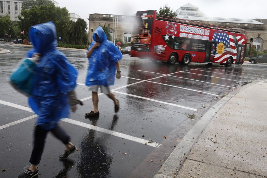 Under ponchos for protection from the steady rain, people walk toward the U.S. Capitol as a tourist bus speeds away while the first bands of Hurricane Irene make their way into Washington Saturday, Aug 27, 2011. (AP Photo/Jacquelyn Martin)