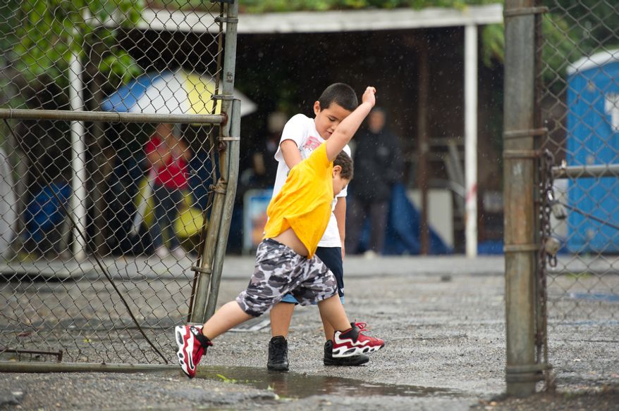 Six-year-old Juan Fuentes helps his little brother, 4 year old Dannie Fuentes, jump over a puddle along Florida Avenue, NW, Washington, DC, Sunday, August 28, 2011. (Andrew Harnik / The Washington Times)