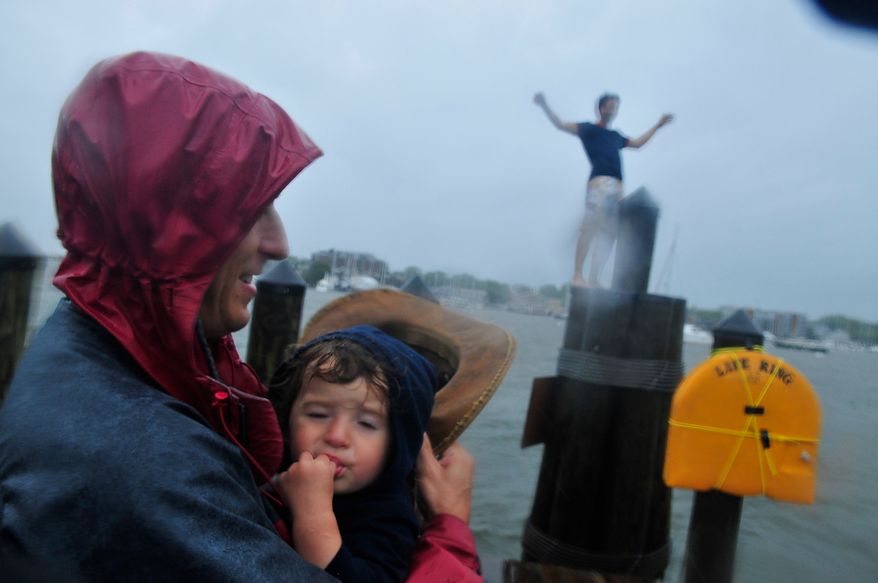 Ben Farrell holds his daughter Nico Farrell, 18 months along City Dock as bands of high winds and heavy rain from Hurricane Irene lash Annapolis, Md., Saturday, August 27, 2011. In background, Jordan Crabtree, of Annapolis, Md., climbs a pier mooring on City Dock. (J.M. Eddins, Jr./The Washington Times)