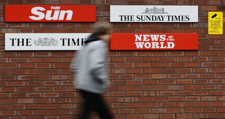**FILE** In this photo from Jan. 27, 2011, a pedestrian passes signs at the entrance to News International in Wapping, London. (Associated Press)