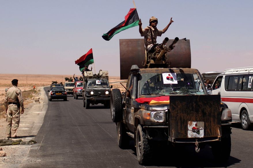 Associated Press photographs
Above: Libyan rebels head to the front line Thursday through the last checkpoint before Bani Walid, Libya. Thousands of rebels have converged on Bani Walid and have threatened to attack if residents don't surrender by Saturday. A number of regime loyalists are thought to be in Bani Walid. Top: A rebel removes Gadhafi slogans from a roadside sign.