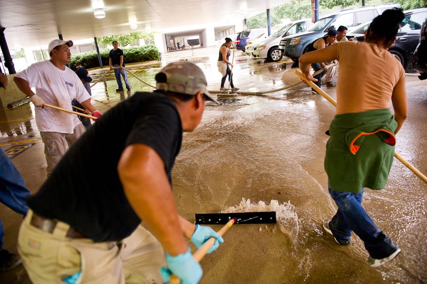 A cleaning crew removes mud from an office building's parking lot on Eisenhower Avenue in Alexandria, Va., on Sept. 9, 2011. The lot was flooded after heavy rains pounded the region the previous night. (Andrew Harnik/The Washington Times)