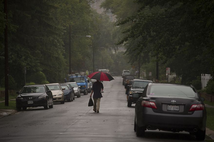 A man walks Sept. 9, 2011, in a steady rain through Arlington Terrace in the Huntington neighborhood of Alexandria, Va., as residents attempted to clean up after heavy rains flooded the area. (Rod Lamkey Jr./The Washington Times)