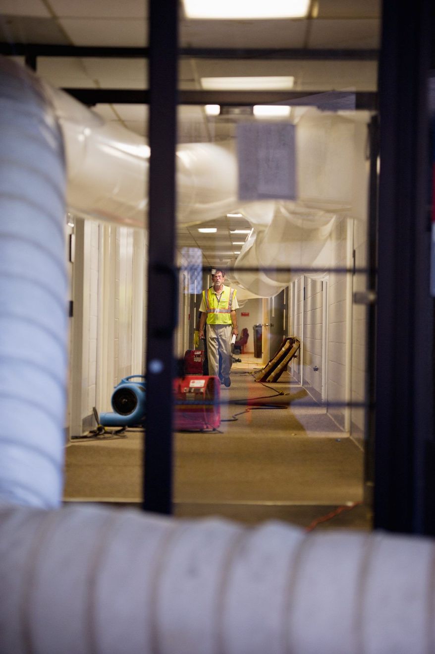 A worker walks along large dehumidifying tubes (top) that were pulling the moisture out of the flooded Prince George's County Administration Building. The building is expected to reopen Tuesday. (Andrew Harnik/The Washington Times)
