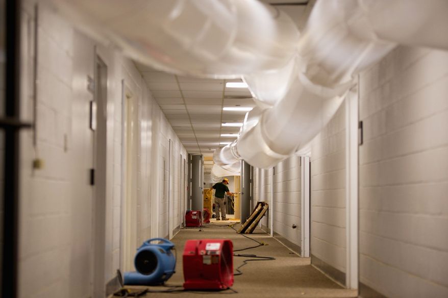 A worker labors in a hallway of the administration building in Prince George's County as large dehumidifying tubes do their work in drying out the building for an expected reopening on Tuesday. (Andrew Harnik/The Washington Times)