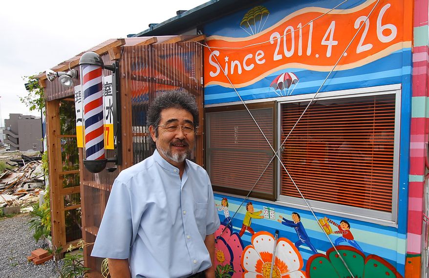 Yasuo Shimizu stands beside his colorful new barber shop in the devastated port area of Ofunato, Japan. The paintings on the shop depict volunteers who helped relief and recovery efforts. (Christopher Johnson/Special to The Washington Times)