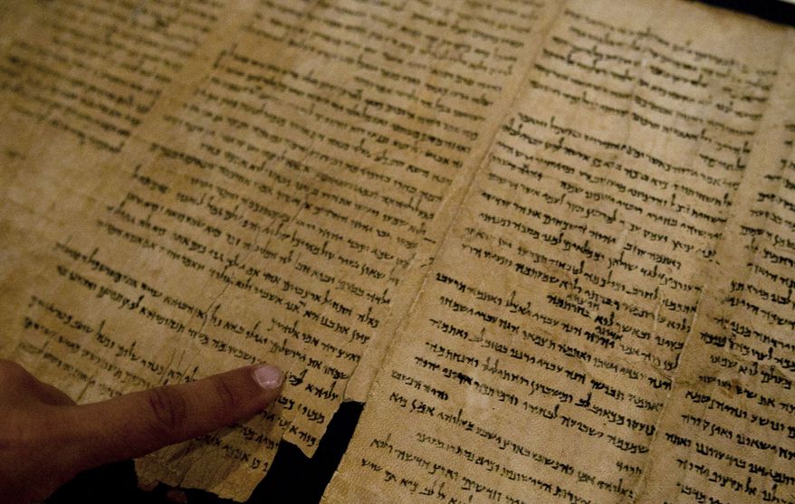 An Israel Museum worker points at the word "Jerusalem" written in a part of the Isaiah Scroll, one of the Dead Sea Scrolls, inside the vault of the Shrine of the Book building at the Israel Museum in Jerusalem on Sept. 26, 2011. (Associated Press)