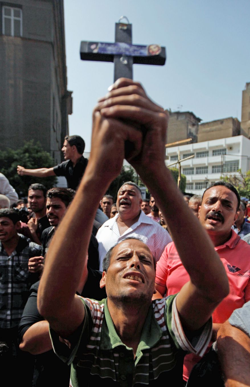 An Egyptian relative of one of the Copts killed during clashes with the Egyptian army late Sunday holds a cross (left) as others chant angry slogans during a gathering outside a morgue. (Associated Press)