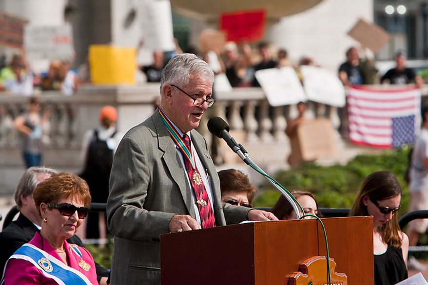 Col. Thomas J. Hogan, head of the National Columbus Celebration Association, leads a Columbus Day celebration and wreath presentation as protesters shout and wave signs in the background at Union Station in Washington on Monday, Oct. 10, 2011. (T.J. Kirkpatrick/The Washington Times)