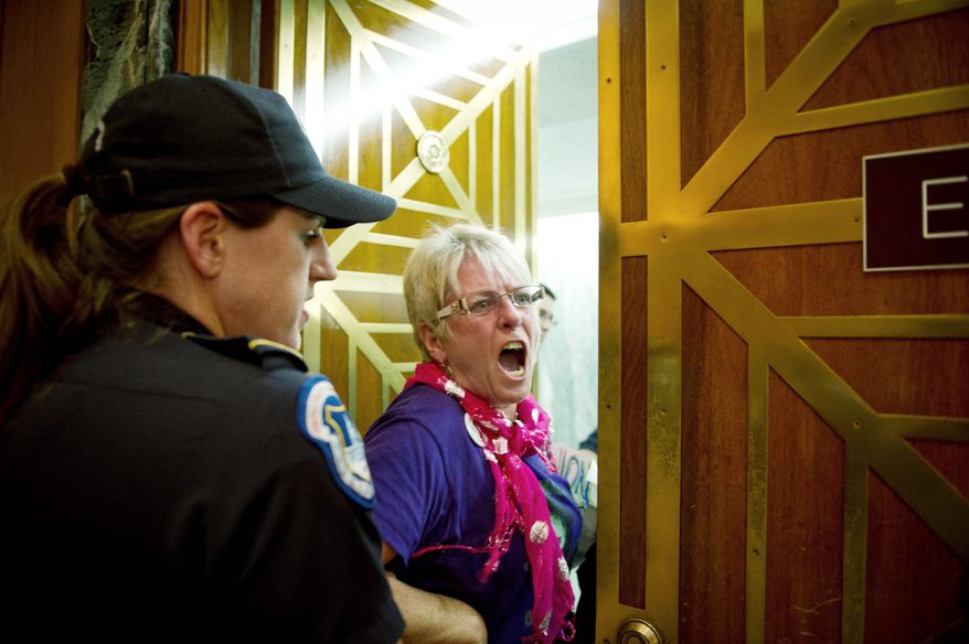 A protester is removed Tuesday from the Senate Finance Committee's markup of trade agreements with South Korea, Colombia and Panama on Capitol Hill. Congress is expected to pass the pacts Wednesday. (Rod Lamkey Jr./The Washington Times)