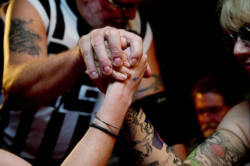 Referee Philip Yunger holds two arm-wrestlers' hands in place as they prepare to clash. (Barbara L. Salisbury/The Washington Times)