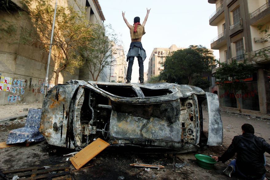 A protester stands on top of a burned car during clashes with Egyptian riot police, unseen, in Tahrir Square in Cairo on Monday. Security forces fired tear gas and clashed with several thousand protesters in the third straight day of violence that has killed at least two dozen people and has become the most sustained challenge yet to the rule of Egypt's military. (Associated Press)