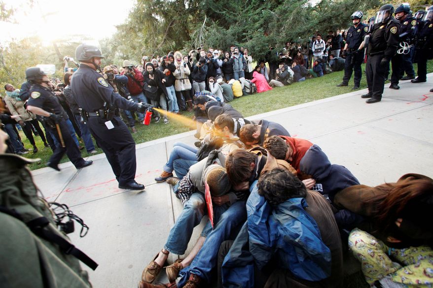 A University of California, Davis police officer uses pepper spray to move Occupy UC Davis protesters while blocking their exit from the school's quad in Davis, Calif., on Friday. Two were hospitalized. The pictures of the incident went viral over the weekend, and UC Davis authorities apologized Monday. (Associated Press)