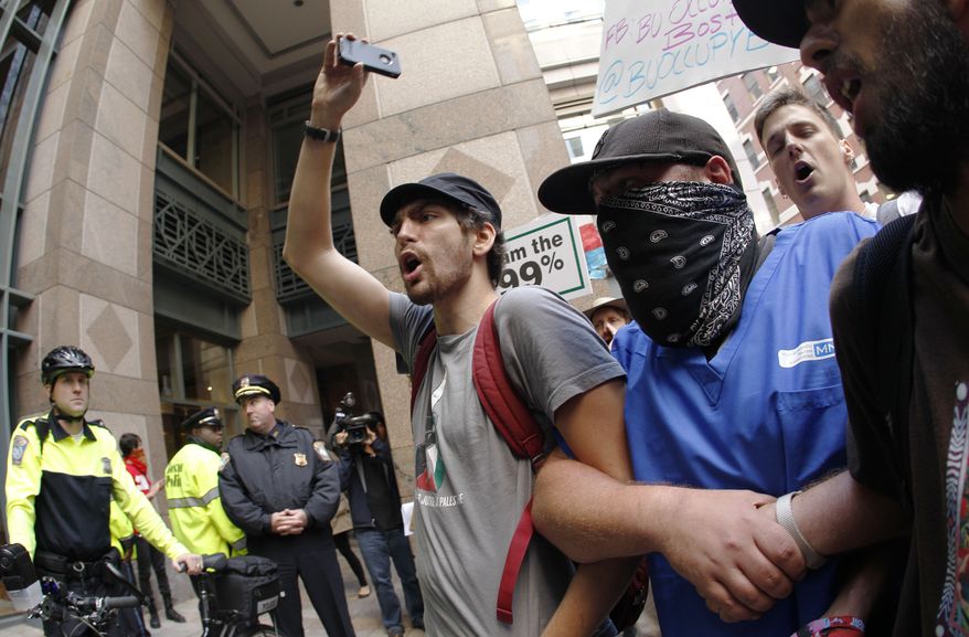 **FILE** Occupy Boston protesters gather Oct. 5, 2011, outside a building in the Financial district in Boston as law enforcement officials look on at left. (Associated Press)