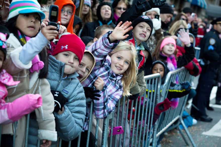 Young spectators wave to Santa Claus as he rolls down 7th Avenue during the Macy's Thanksgiving Day Parade. (AP Photo/John Minchillo)