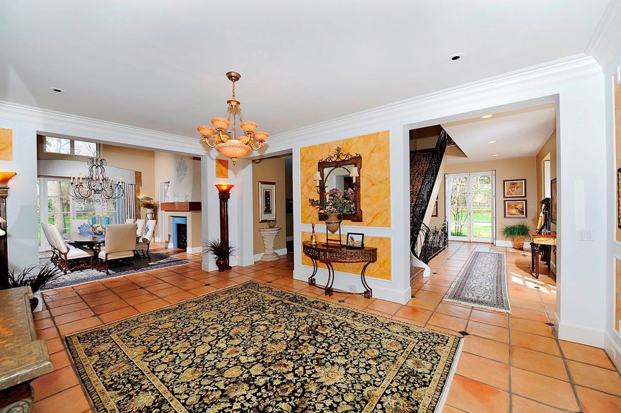 The front walkway leads into a grand reception hall with terra-cotta tile flooring, a chandelier and recessed lighting.
