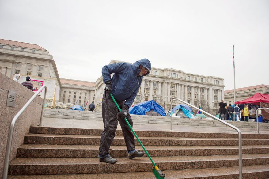 With the John A. Wilson Building looming in the distance, Charles Holsopple helps keep the area clean at the Stop the Machine protest encampment at Freedom Plaza in Washington on Thursday. Mr. Holsopple, 58, left his home in Tampa Bay, Fla., to join the movement and has been here since Oct. 6. (Rod Lamkey Jr./The Washington Times)