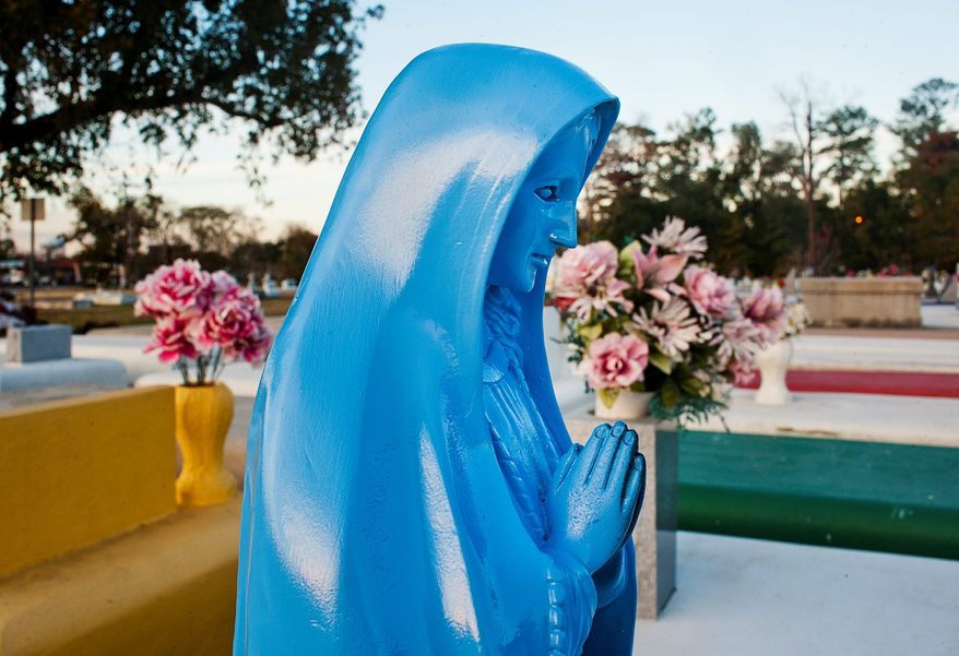 A blue statue of the Virgin Mary is surrounded by yellow, green and red grave markers at the Southdown Cemetery in Houma, La. Local lawmaker Alvin Tillman is pushing for legislation that would make it illegal to paint a tomb anything but white. (Houma Courier via Associated Press)