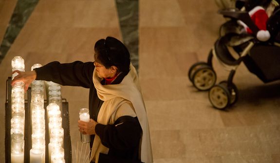 A woman lights a candle during Christmas Mass celebrated by Archbishop of Washington Cardinal Donald Wuerl at the Basilica of the National Shrine of the Immaculate Conception on Christmas Day, Washington, D.C., Sunday, Dec. 25, 2011. (Andrew Harnik/The Washington Times)