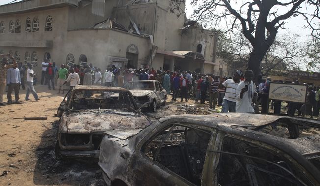 Onlookers gather around a destroyed car at the site of a bomb blast at St. Theresa Catholic Church in Madalla, Nigeria, on Sunday, Dec. 25, 2011. (AP Photo/Sunday Aghaeze)

