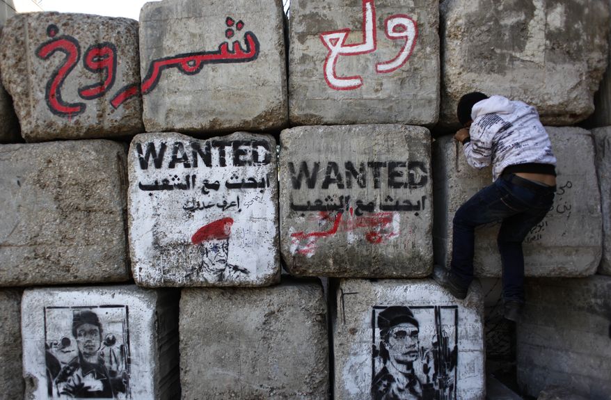 **FILE** An Egyptian child climbs cement blocks used to separate police forces from demonstrators Dec. 8, 2011, at the site of recent clashes in Cairo's Tahrir Square between police and demonstrators that left more than 40 people dead. The graffiti on the blocks depicts a police officer accused of targeting the eyes of protesters. (Associated Press)
