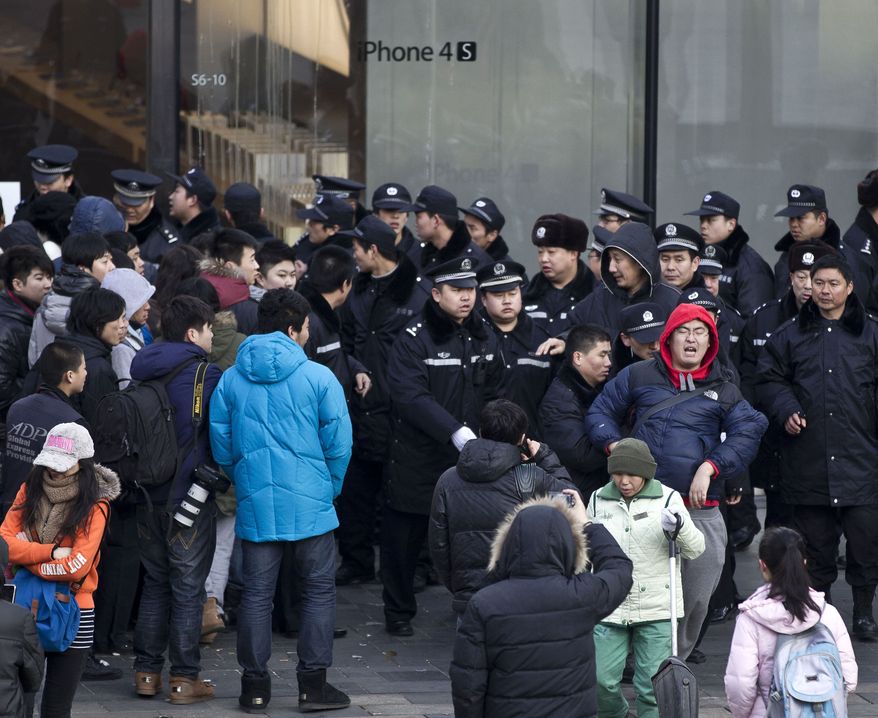 A man in a red hood reacts Jan. 13, 2012, after being pushed away by police officers for refusing to leave Apple's Beijing flagship store, as stains of eggs are left on its glass wall in the background. An angry crowd shouted and threw eggs at the store after it failed to open on schedule to sell the popular smartphones. (Associated Press)
