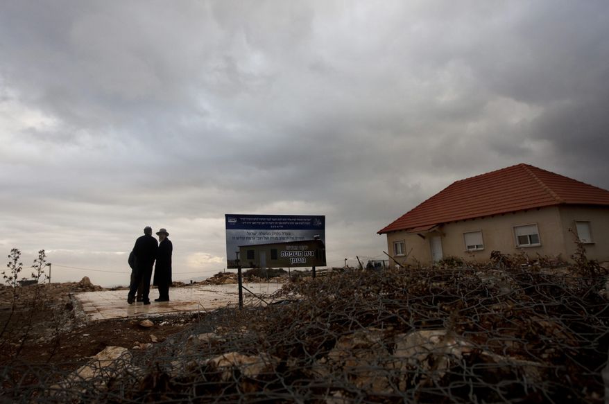 In this photo taken Monday, Jan. 23, 2012, Jewish settlers walk near the remaining foundations of a demolished house, with a sign wishing its rebuilding, in the unauthorized West Bank Jewish settlement of Migron. (AP Photo/Sebastian Scheiner)