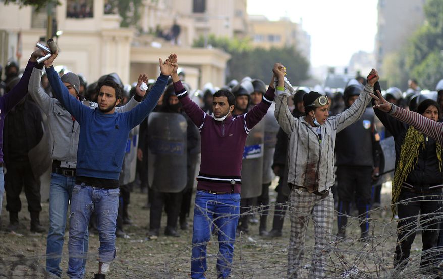Egyptian protestors stand Feb. 3, 2012, in front of riot police to stop others from throwing stones during clashes near the Interior Ministry in downtown Cairo. A volunteer doctor says police and protesters angry over a deadly soccer riot have clashed for the second day in the Egyptian capital, and that one man died in the latest violence. (Associated Press)