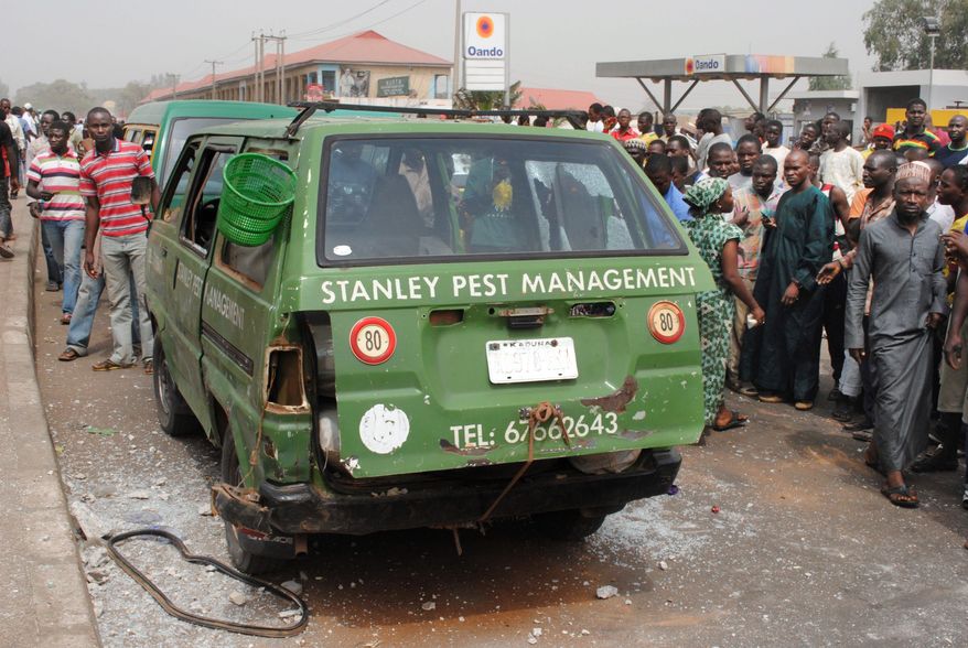 Nigerians gather around a minibus struck by an apparent explosion near a highway overpass in Kaduna on Tuesday. Two larger explosions struck near army and air force bases on the outskirts of the city. (Associated Press)