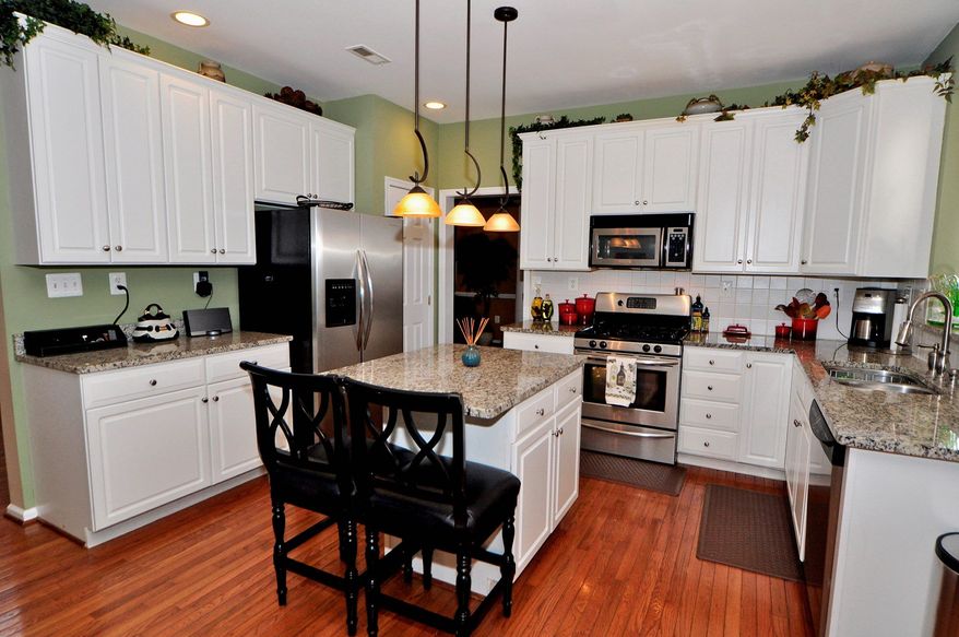 The kitchen has a center island and breakfast bar, granite counters, white cabinetry and stainless steel appliances.