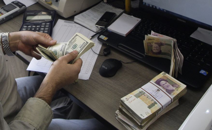 **FILE** A currency exchange bureau worker counts U.S. dollars, as Iranian bank notes are seen at right with portrait of late revolutionary founder Ayatollah Khomeini, in downtown Tehran on Dec. 21, 2011. (Associated Press)