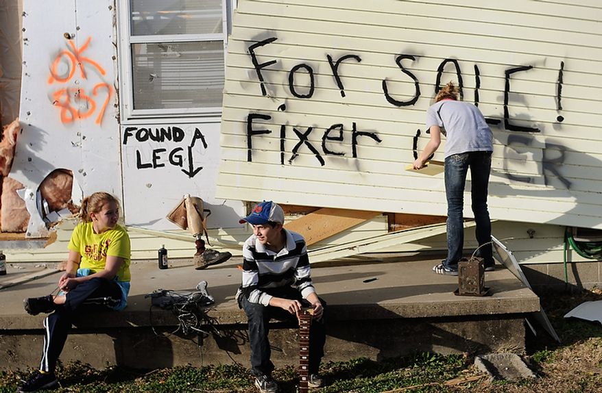 From left, Alli Ferrell, 10, and cousin Christian Murray, 12, sit on the front porch, as Lindsey Murray, 15, of Harrisburg, Ill., paints "for sale fixer upper" on the side of the home of their grandmother, Sharon Murray, 61, after a tornado destroyed the house in Harrisburg, Ill., Wednesday, Feb. 29, 2012. A tornado struck the small town in southern Illinois killing 6. Murray was not at home at the time of the storm. A prosthetic leg was found among the wreckage. (AP Photo/Stephen Lance Dennee)