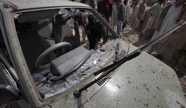 A Pakistani police officer examines a parked car damaged in a suicide bombing in the Badhber area on the outskirts of Peshawar, Pakistan, on Sunday, March 11, 2012. (AP Photo/Mohammad Sajjad)