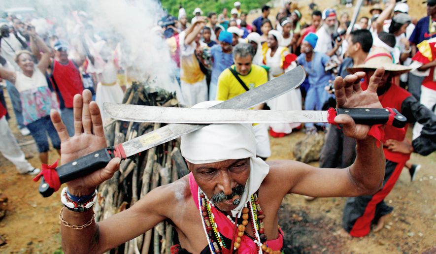 A Santero priest in 2010 holds machetes over his head as he moves around a fire during a Santeria ceremony at the annual Caribbean Festival in Loma del Cimarron, El Cobre, Cuba. (Associated Press) ** FILE **
