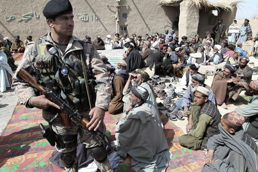An Afghan security guard keeps watch Tuesday as villagers listen to a speech by an Afghan official. They are part of a delegation attending a prayer ceremony for civilian victims in a killing spree Sunday, possibly by a U.S. soldier, in Kandahar province. (Associated Press)